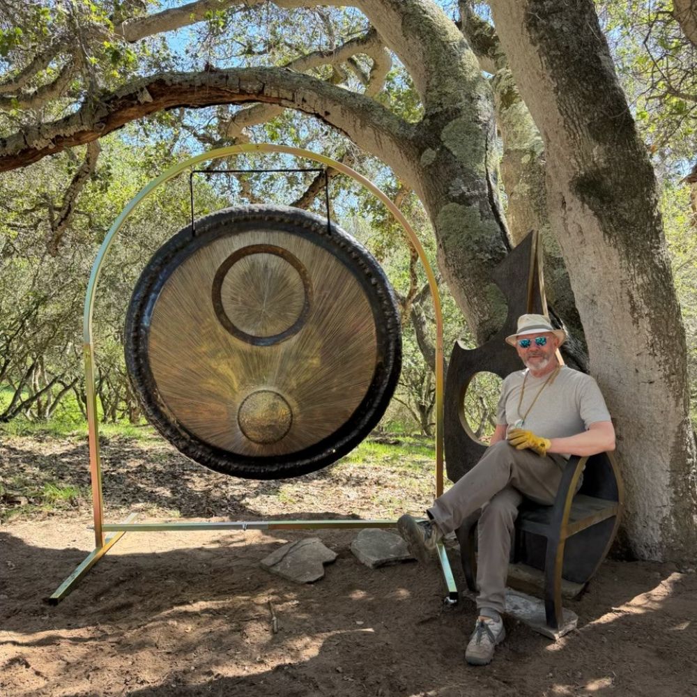 Adron Beene seated under an oak tree next to a very large, brass gong.