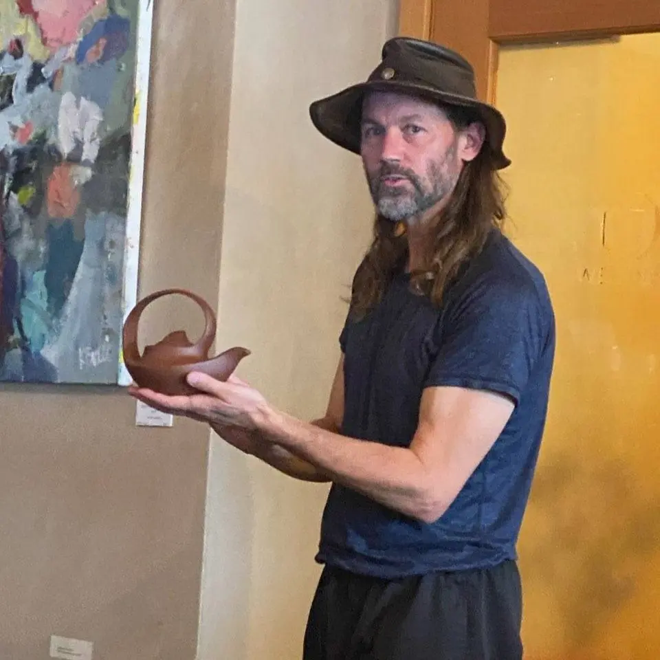 Gideon holding a brown, clay tea pot.