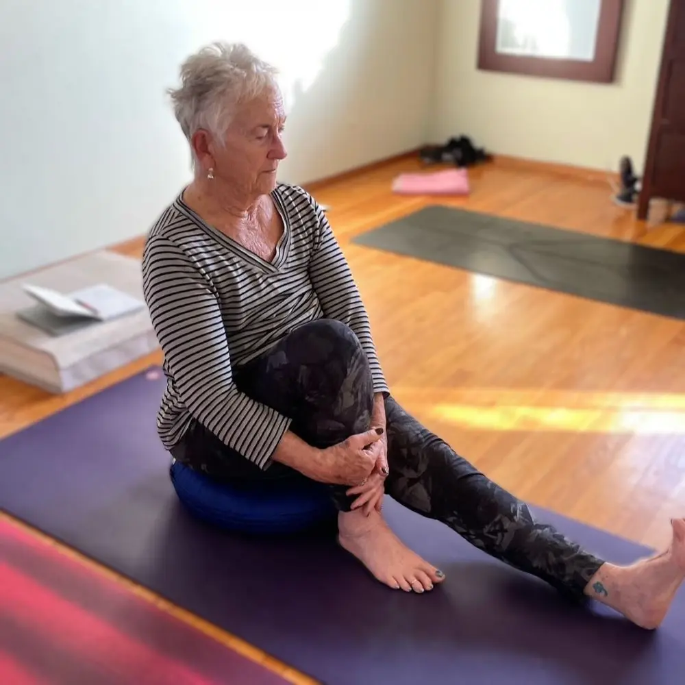 Linda sits on a bolster with one knee to her chest.