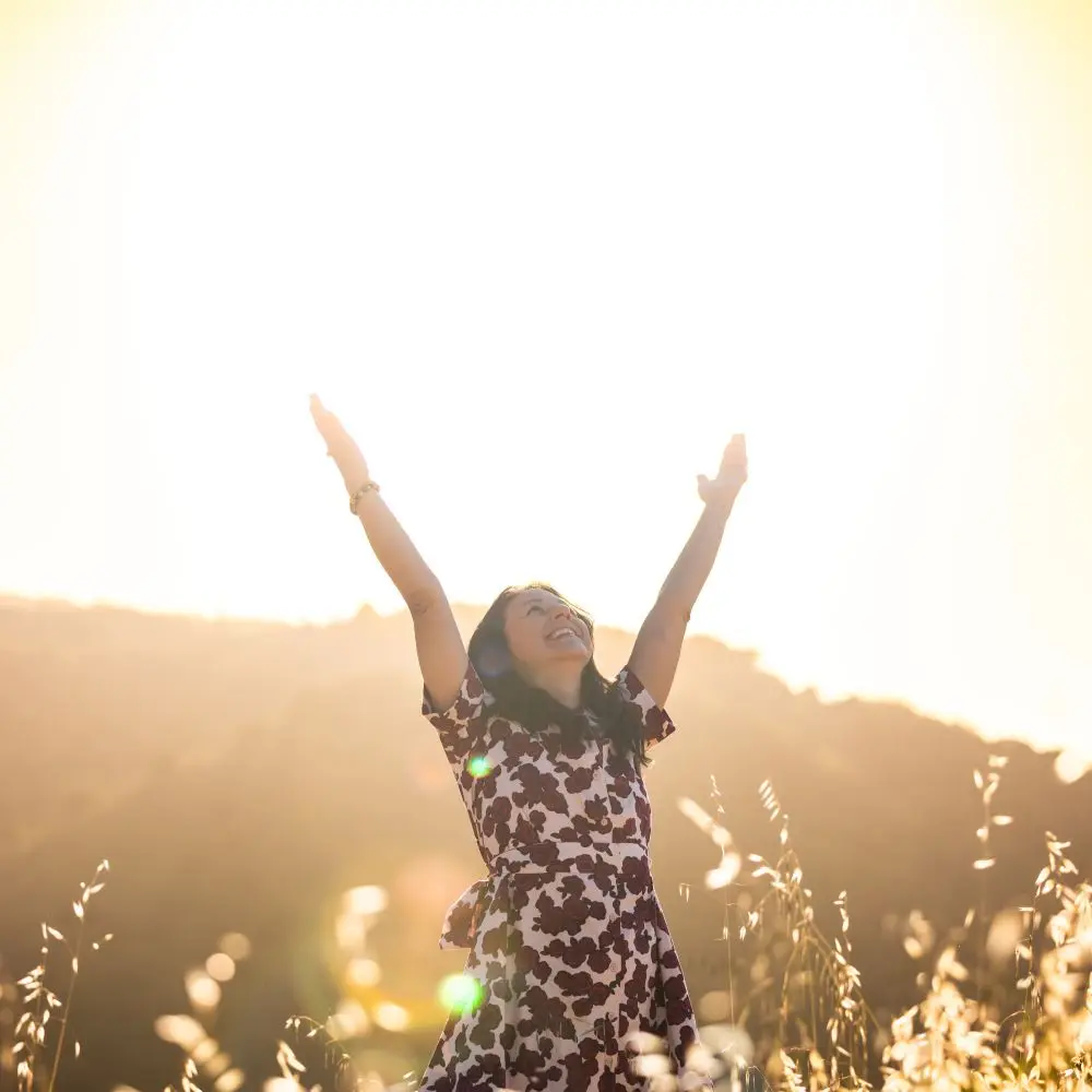 Paulette Sato outdoors, with her arms joyfully up in the air, with a mountain in the backdrop.