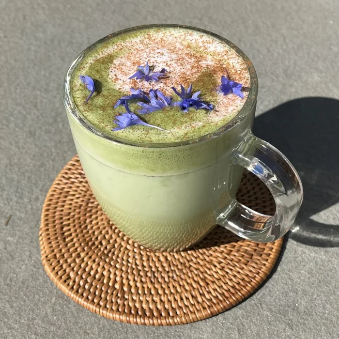 cinnamon honey matcha in a clear cup on a woven coaster