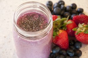 a pink smoothie with chia seeds, with fresh strawberries and blueberries as a garnish