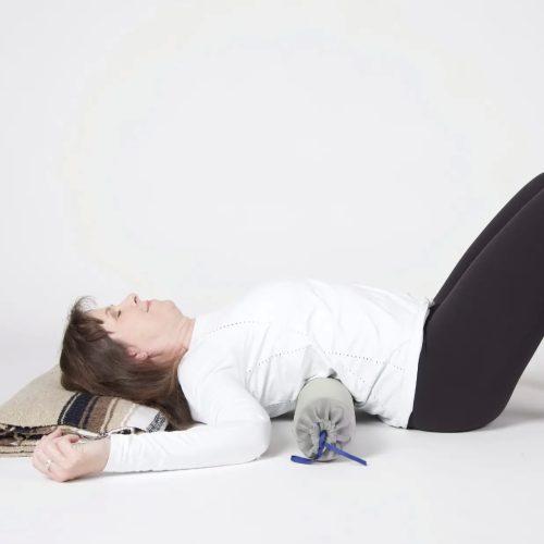 Yoga teacher laying on her back, with knees bent and a support under her head and mid back.