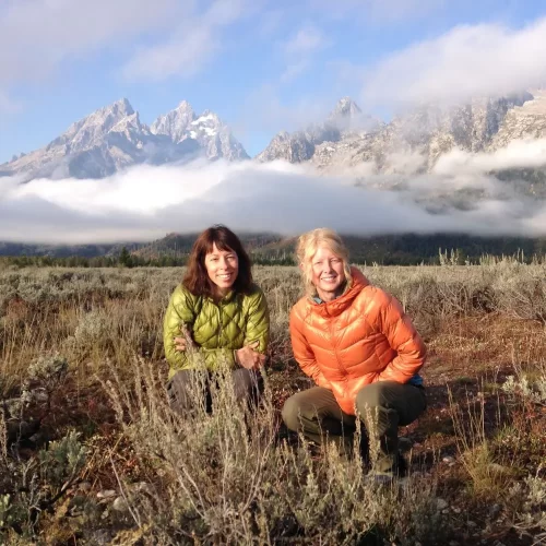 Jill Lacher & Bevie Labrie in a filed with a mountain range behind them.