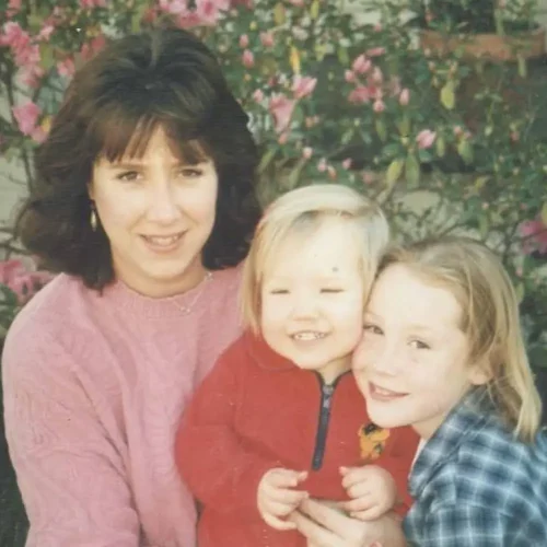 A mother and her two young children smiling outdoors.