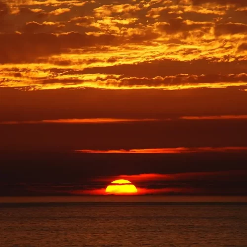 The sun setting by the ocean. The skies are dark reds and oranges.