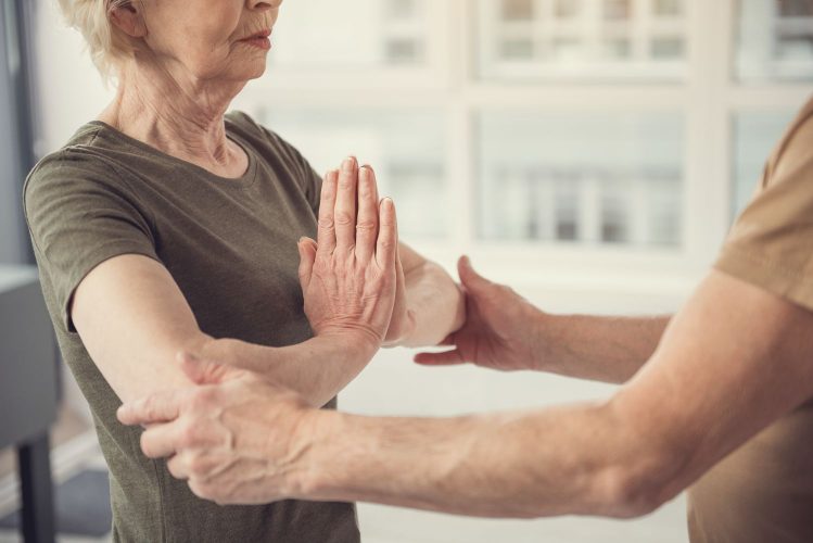 Peaceful old lady with hands clasped at her chest standing in front of a man touching her elbows