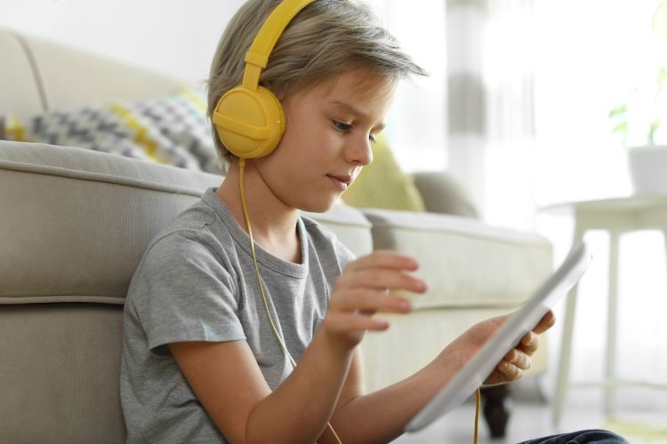 Cute little boy with headphones and tablet listening to audiobook at home