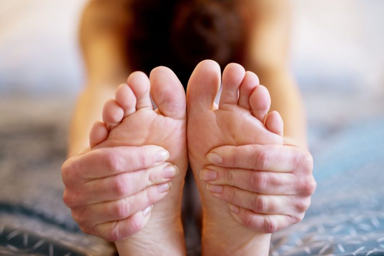 Close up focus view of feet and hands while a fit healthy woman doing yoga stretching on the bed.