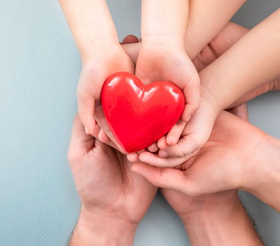 An adult, mother, father and child hold a red heart in their hands. Concept for charity, health insurance, love, international cardiology day.