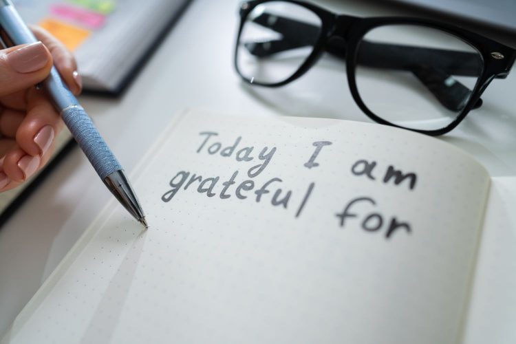 Close-up Of A Person Writing I Am Grateful For Text In Notebook With Black Marker