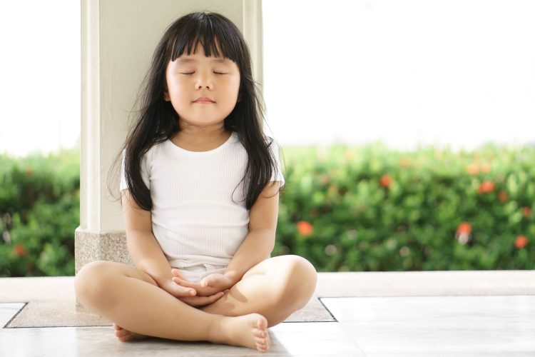 Asian children cute or kid girl sit for meditation with peace and relax in garden pavilion at temple or church and wearing white dress with sunlight on white with space