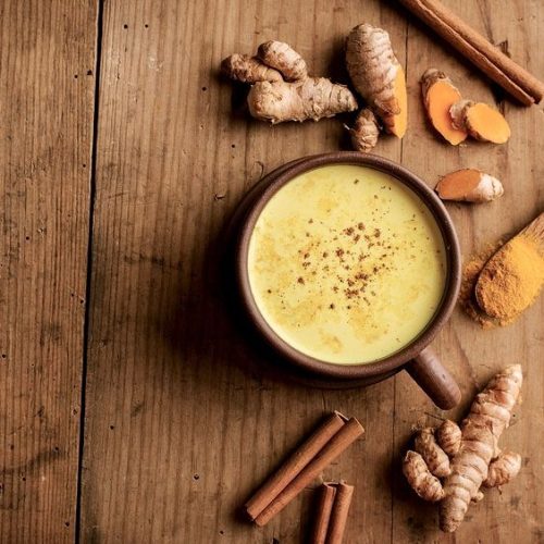 Tasty hot turmeric curcuma milk in cup on old wooden table. Arranged with turmeric roots and spices. View from above with copy space