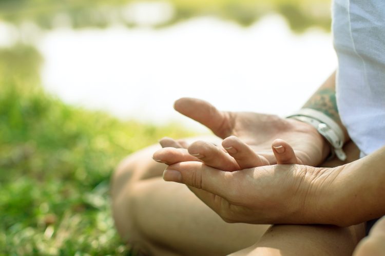 Closeup of kundalini yoga mudra. Female hands of the woman sitting outdoors in yoga pose. Nature is on the background