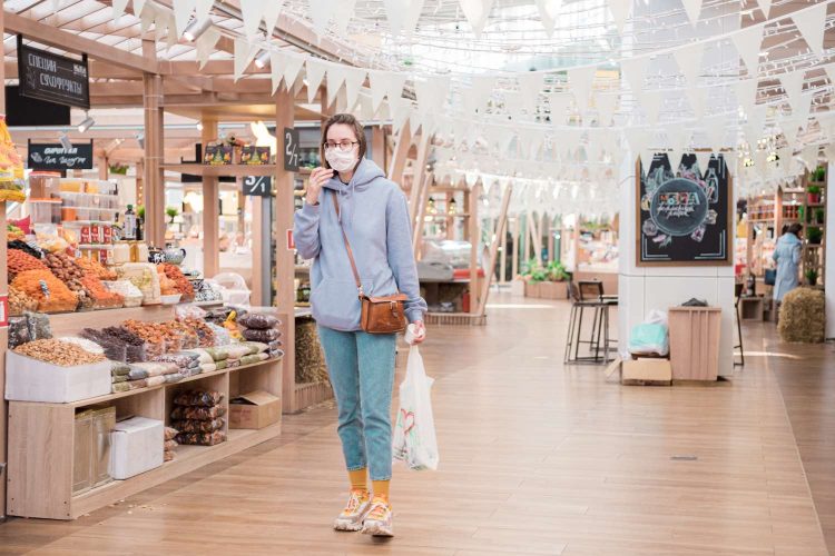 Woman in medical face mask walking in modern food market, shop