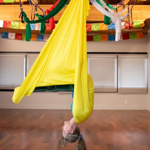 sarah in a yellow aerial hammock doing plow pose