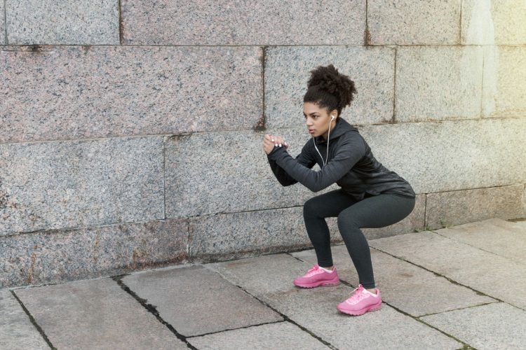 Sporty woman doing warm up squat, stretching near a wall