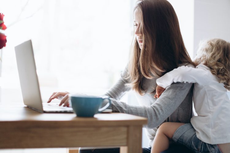 Young mother and her little daughter sitting on kitchen using a laptop