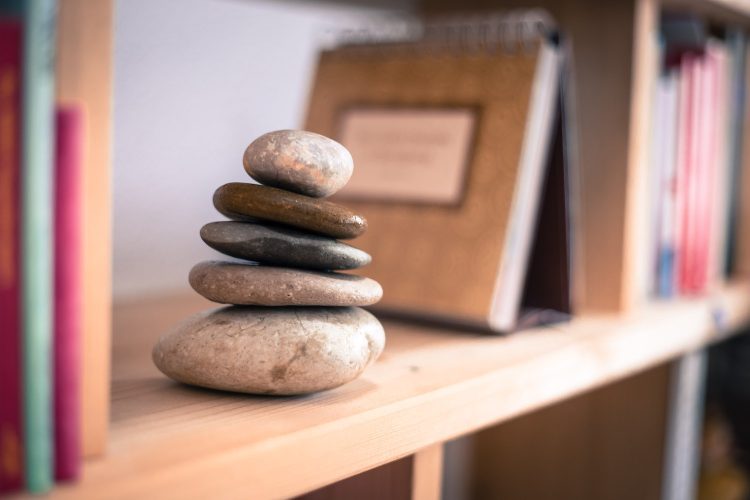 Feng Shui: Stone cairn at home in a book shelf, blurry books in foreground and background. Balance and relaxation.