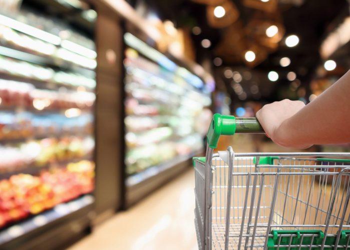 woman hand hold supermarket shopping cart with abstract blur organic fresh fruits and vegetable on shelves in grocery store defocused bokeh light background