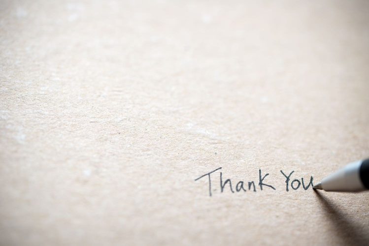 A pen writing the phrase Thank You on a blank paper.