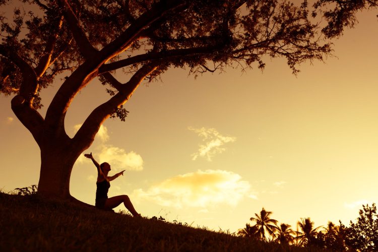 Silhouette of woman with hands raised into the sunset