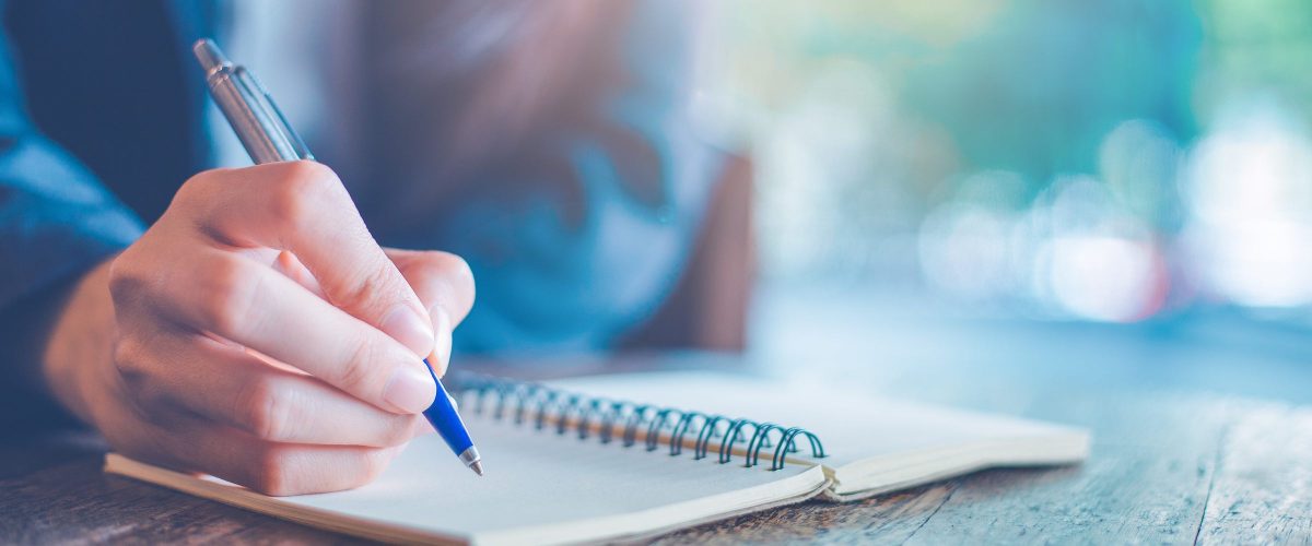 Business woman hand  writing on a notepad with a pen in the office.Web banner.