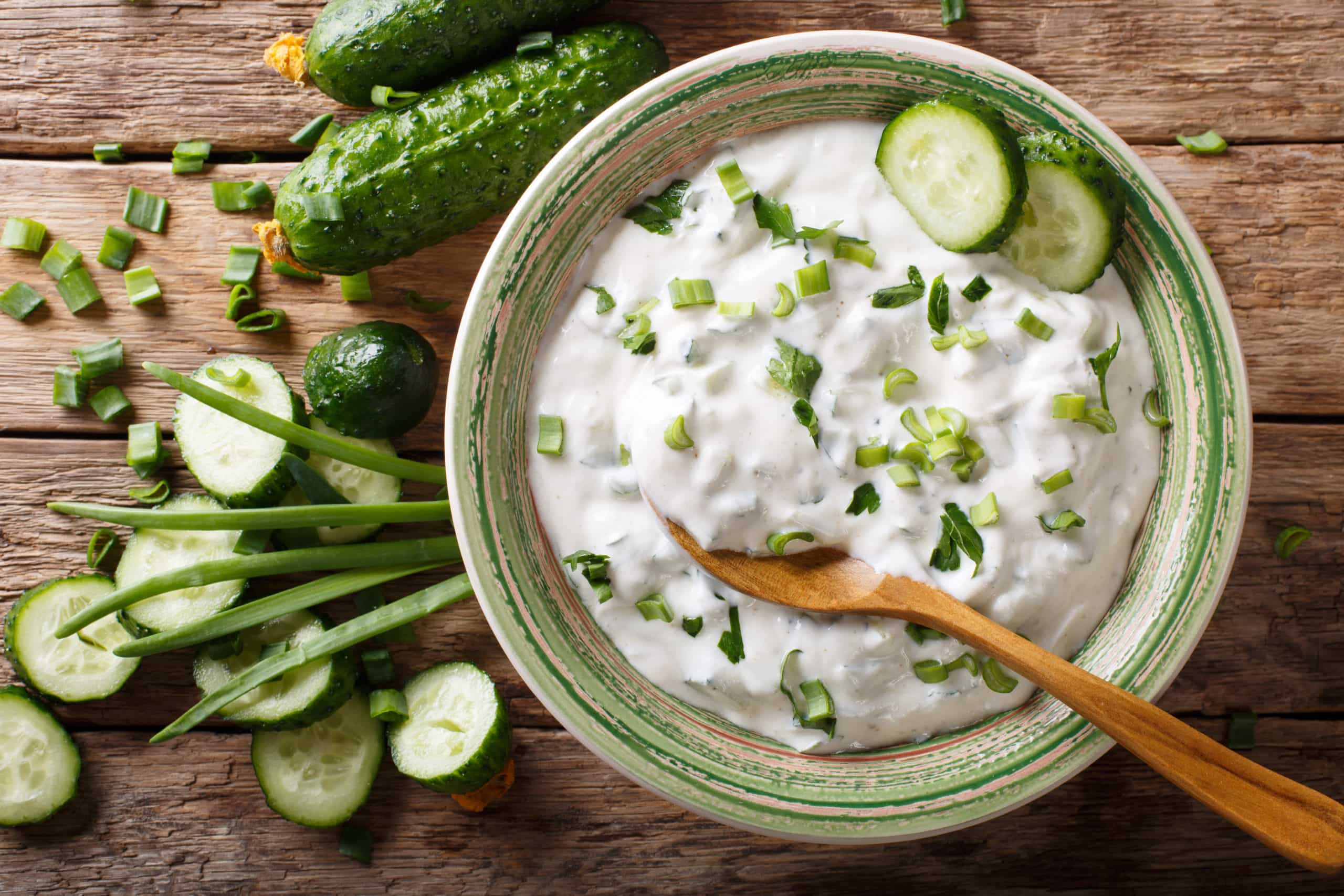 Yogurt-based condiment with herbs, spices and cucumber close-up in a bowl on a table. Horizontal top view from above.