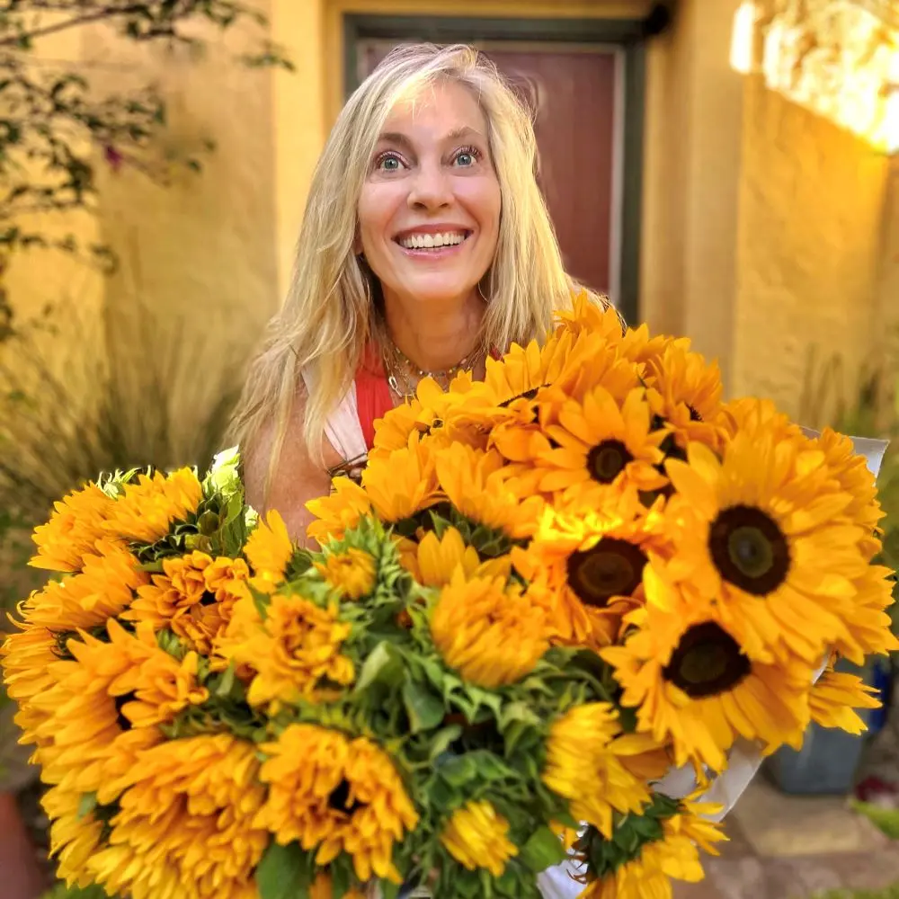 Jennifer Prugh smiling while holding multiple bunches of sunflowers.