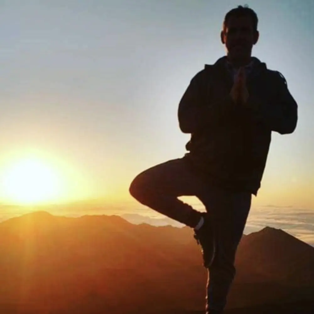Ken McMillian practicing tree pose silhouetted by mountains and a sunrise.