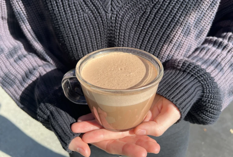 chocolate date latte in a glass mug, held by someone in a cozy sweater