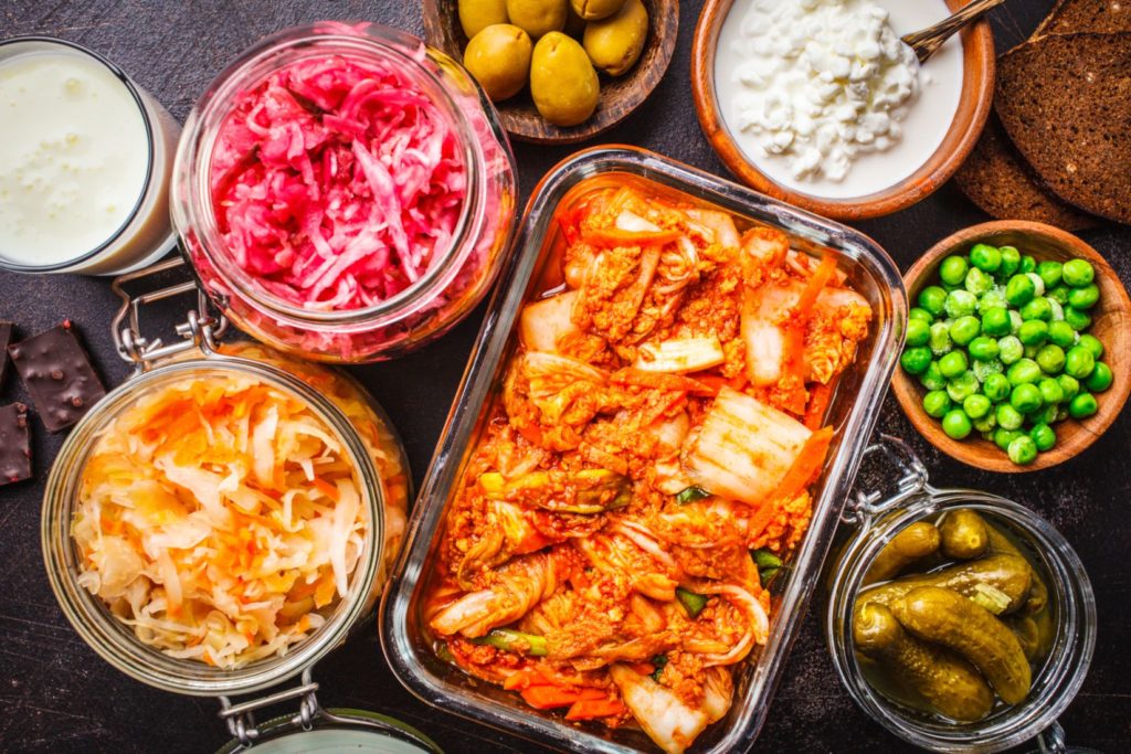 Probiotics food background. Kimchi, beet sauerkraut, sauerkraut, cottage cheese, olives, bread, chocolate, kefir and pickled cucumbers in glass jars, dark background, top view.