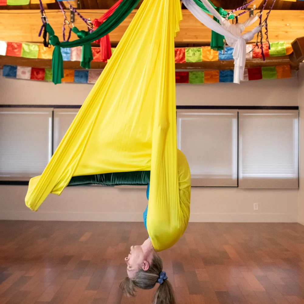 sarah in a yellow aerial hammock doing plow pose